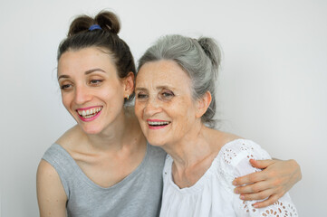 Happy senior mother is hugging her adult daughter, the women are laughing together, sincere family of different age generations having fun on white background, mothers day.