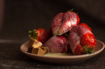 Red ripe strawberries on round plate with a few cane sugar pieces and melted white chocolate