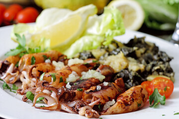Grilled squid with boiled potatoes and chard on white plate. Selective focus