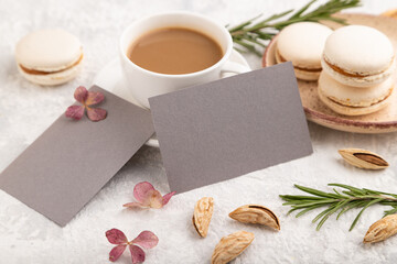 Gray business card mockup with cup of coffee, almonds and macaroons on gray concrete background. side view