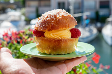 Hand with Tarte tropezienne or La Tarte de Saint-Tropez - dessert pastry consisting of filled brioche with cream and fresh berries.