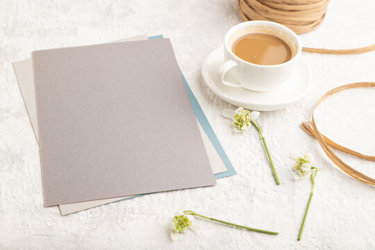 Gray paper sheet mockup with spring snowdrop galanthus flowers and cup of coffee on gray concrete background. side view, close up.