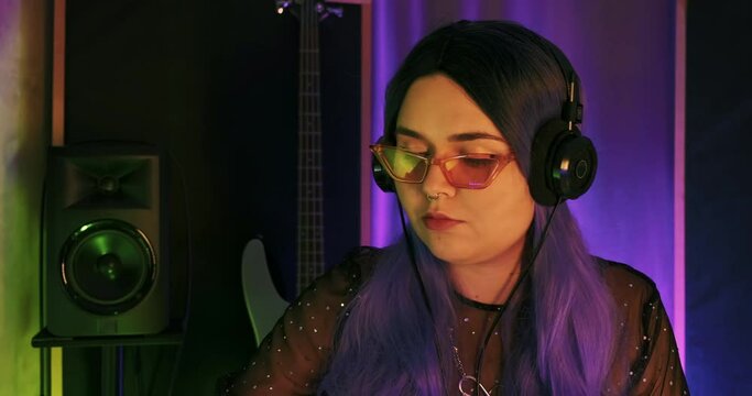 Close-up of female LGBTQ non-binary Dj musician vibing while writing hip-hop edm electronic beats on push midi controller synth in studio. music session online streaming composer, festival moody vibe
