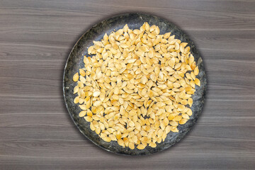 Toasted and salted pumpkin seeds in stone dish on wooden table top view