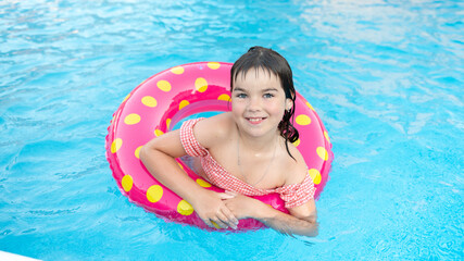 Fototapeta na wymiar cute smiling girl in a bright circle swims on the background of a blue pool in summer. High quality photo