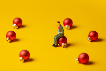 Miniature figure of man sits on Christmas bauble on yellow background