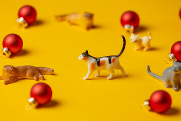 miniature cats figure next to red Christmas baubles on yellow background