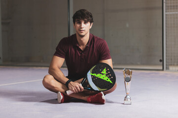 a young paddle tennis player sitting with a trophy after winning a competition.
winner.