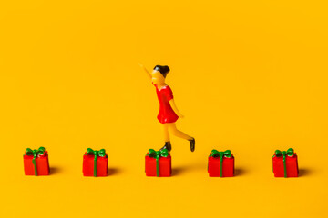 miniature girl figure jumping on red Christmas gift boxes on yellow background