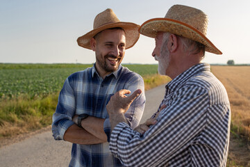 Two farmers standing on road next to field talking laughing.
