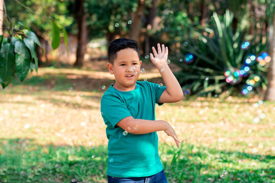 chubby friendly little boy plays with soap bubbles outdoors, nature in the background