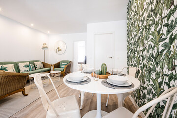 Small round white dining table with service set surrounded by decorative accessories similar to plants and leaves in a vacation rental apartment