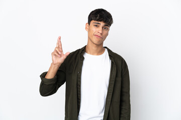 Young man over isolated white background with fingers crossing and wishing the best