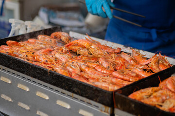 Chef cooking fresh red langoustine shrimps, prawns on grill at summer local food market - close up. Outdoor cooking, barbecue, gastronomy, seafood, cookery, street food concept
