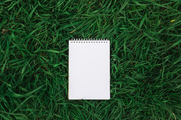 Notebook or white sketch book mock up on green grass. Copy space, top view, place for text, flat lay. Nature, ecology, summer, zero waste lifestyle, organic concept