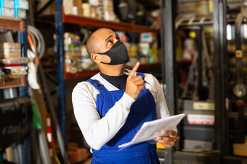 Warehouse manager in protective mask calculates the quantity of goods and writes it down in a notebook