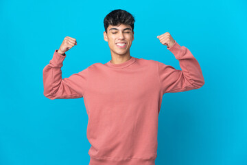 Young man over isolated blue background doing strong gesture