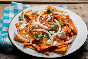 Mexican food. Red chilaquiles with cheese and sour cream on wooden background