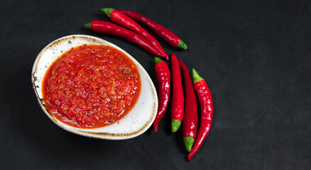 Paste harissa sauce in a bowl on a black background close up. Adjika hot chili peppers sauce. Copy...