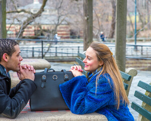 A girl and a guy are sitting crossing a table, smilingly looking at each other, with a leather bag..