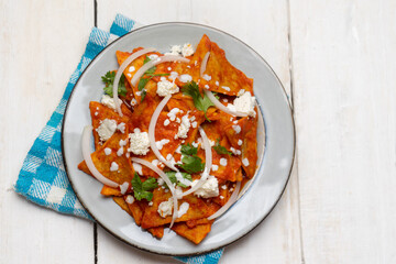 Mexican food. Red chilaquiles with cheese and sour cream on white background