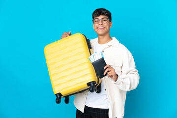 Young man over isolated blue background in vacation with suitcase and passport