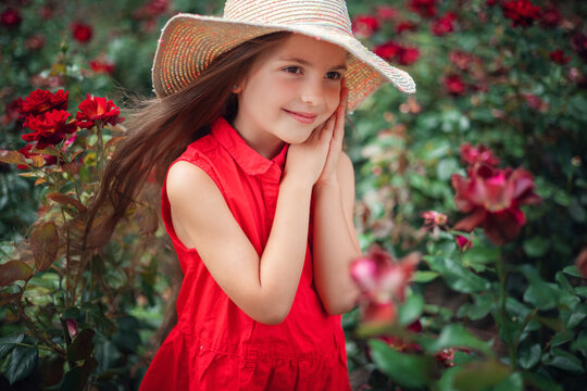Beautiful little girl in roses garden in park. Charming woman smiling outdoor with flowers.