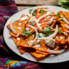 Mexican food. Red chilaquiles with cheese and sour cream on wooden background