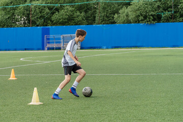 The boy loves to play football, trains with the ball on the artificial turf and scores a goal. The boy plays football