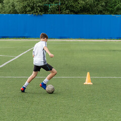 The boy loves to play football, trains with the ball on the artificial turf and scores a goal. The boy plays football