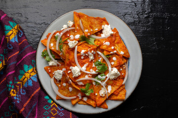 Mexican food. Red chilaquiles with cheese and sour cream on dark background