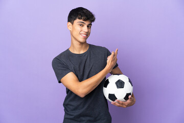 Young football player man over isolated purple background pointing back
