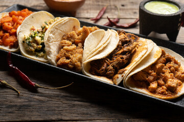 Different types of tacos also called guisados on a wooden background. Mexican food