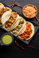 Different types of tacos also called guisados on a dark background. Mexican food