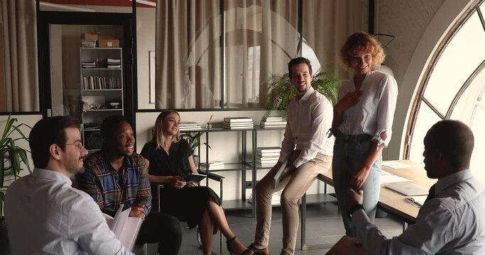 Six diverse employees participate at briefing lead by middle-aged woman in modern office. Group of multi racial colleagues share ideas offer for project development, friendly conversation at workday