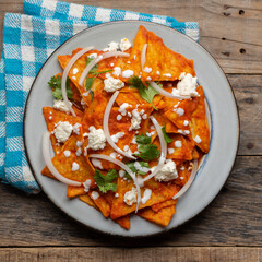 Mexican food. Red chilaquiles with cheese and sour cream on wooden background