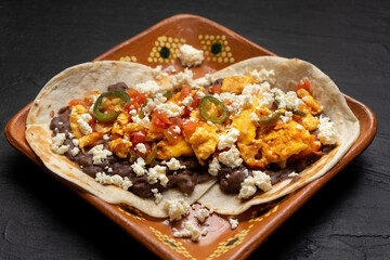 Mexican eggs with refried beans and cheese on dark background.