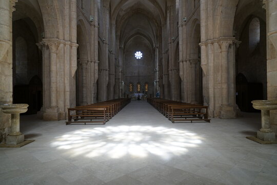 navata centrale semibuia di una abbazia medievale con il pavimento illuminato dal riflesso del rosone