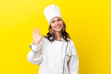 Young Russian chef girl isolated on yellow background saluting with hand with happy expression