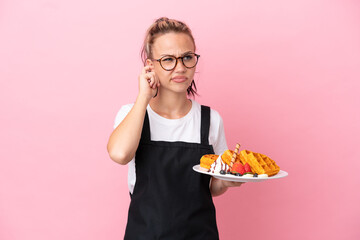 Restaurant waiter Russian girl holding waffles isolated on pink background frustrated and covering ears