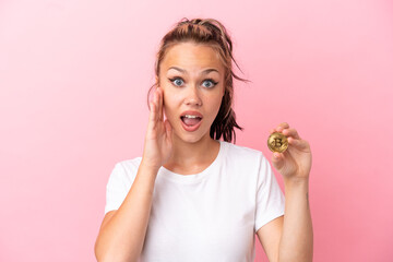 Teenager Russian girl holding a Bitcoin isolated on pink background with surprise and shocked facial expression