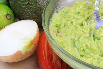 Bowl full of guacamole with the ingredients around 