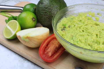 Bowl full of guacamole with the ingredients around 