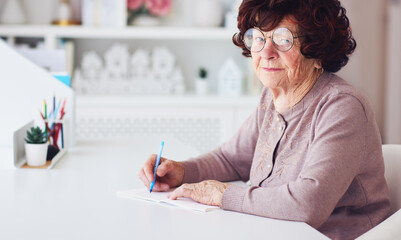 cheerful senior woman sitting at the desk, writting notes, 84 years old lady