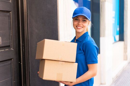 Young delivery woman at outdoors holding boxes with happy expression