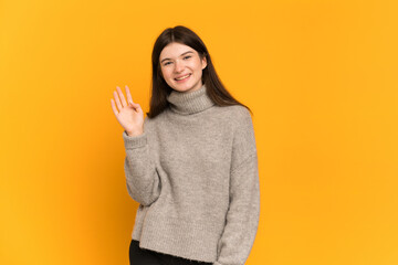 Young Ukrainian girl isolated on yellow background saluting with hand with happy expression
