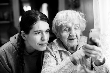 An senior woman looks at a smartphone, with his adult granddaughter. Black and white photo.