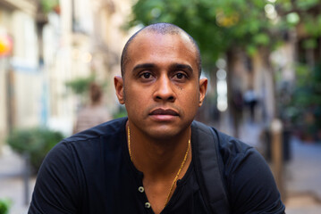 Closeup portrait of focused adult hispanic man in black long sleeve shirt with backpack on shoulder on city street