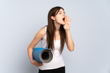 Young Ukrainian sport girl going to yoga classes while holding a mat shouting with mouth wide open to the side