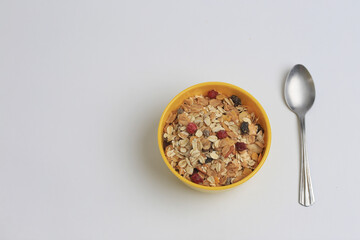 Toma Superior de Plato de granola amarillo sobre fondo Blanco junto a cuchara plateada. Granola y Avena en Plato hondo y sin leche. 